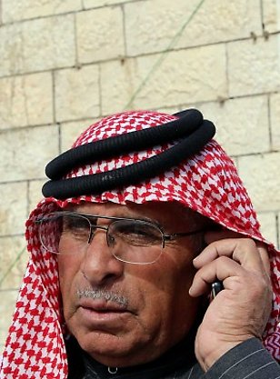 FILE - In this Jan. 3, 2015 file photo, Safi Yousef al-Kaseasbeh, the father of the Jordanian pilot 1st Lt. Mu'ath al-Kaseasbeh, speaks on his mobile phone, while standing by a poster of his son at a gathering of his family in Karak, south of Amman, Jordan. An online video released Tuesday, Feb. 3, 2015 purportedly shows a Jordanian pilot captured by the Islamic State extremist group being burned to death. The Associated Press was not immediately able to confirm the authenticity of the video, which was released on militant websites and bore the logo of the extremist group's al-Furqan media service. (AP Photo/Raad Adayleh, File) Foto: Ap